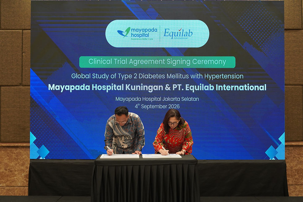 Two people sign documents at a clinical trial agreement ceremony for Mayapada Hospital and Equilab on a blue stage backdrop.